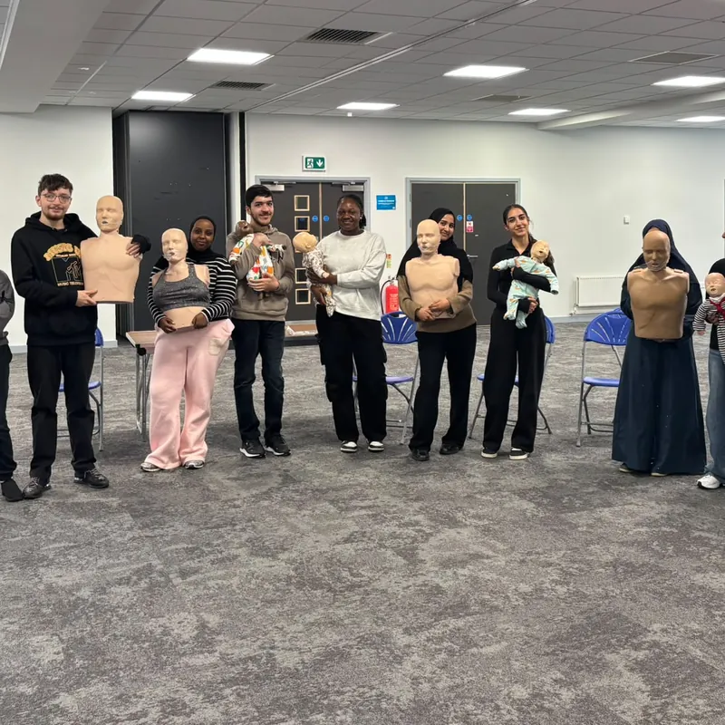 A training group holding adult, child and baby CPR manikins