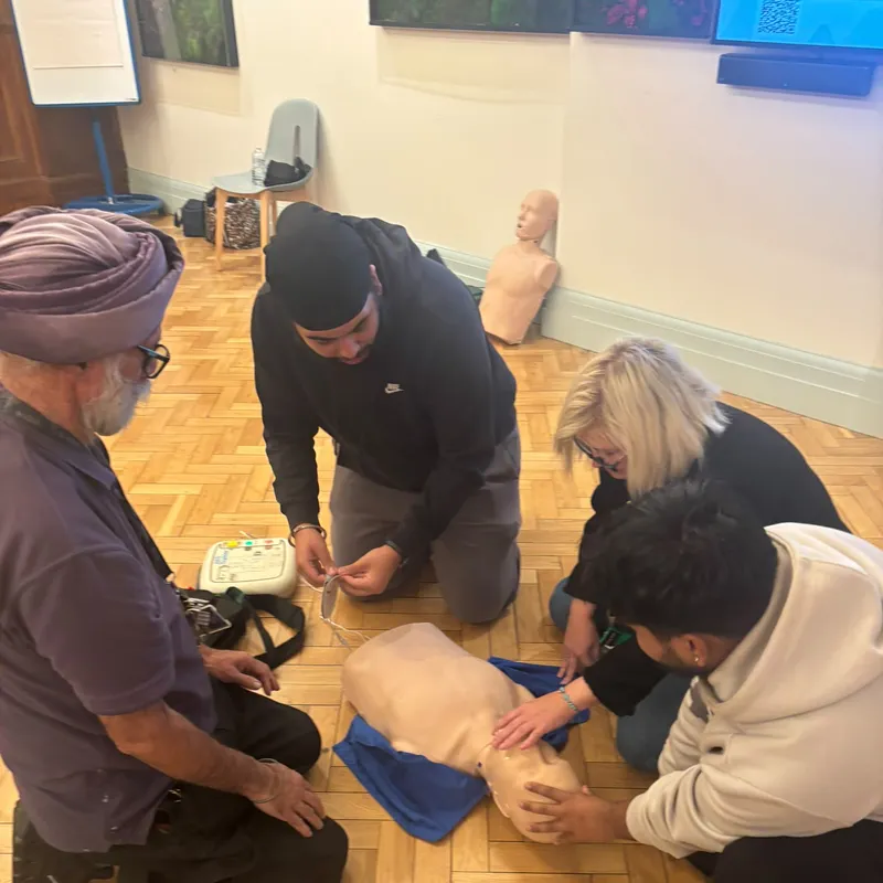 A group kneeling round a CPR manikin while one prepares the AED trainer pads