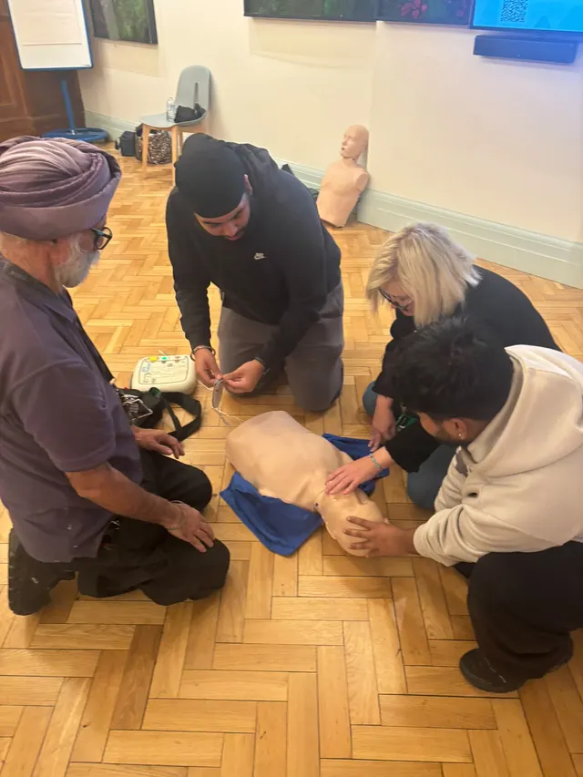 A group kneeling round a CPR manikin while one prepares the AED trainer pads