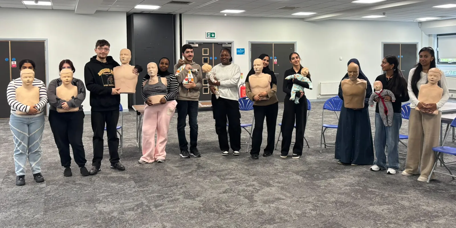 A training group standing in a line holding adult, child and baby CPR manikins
